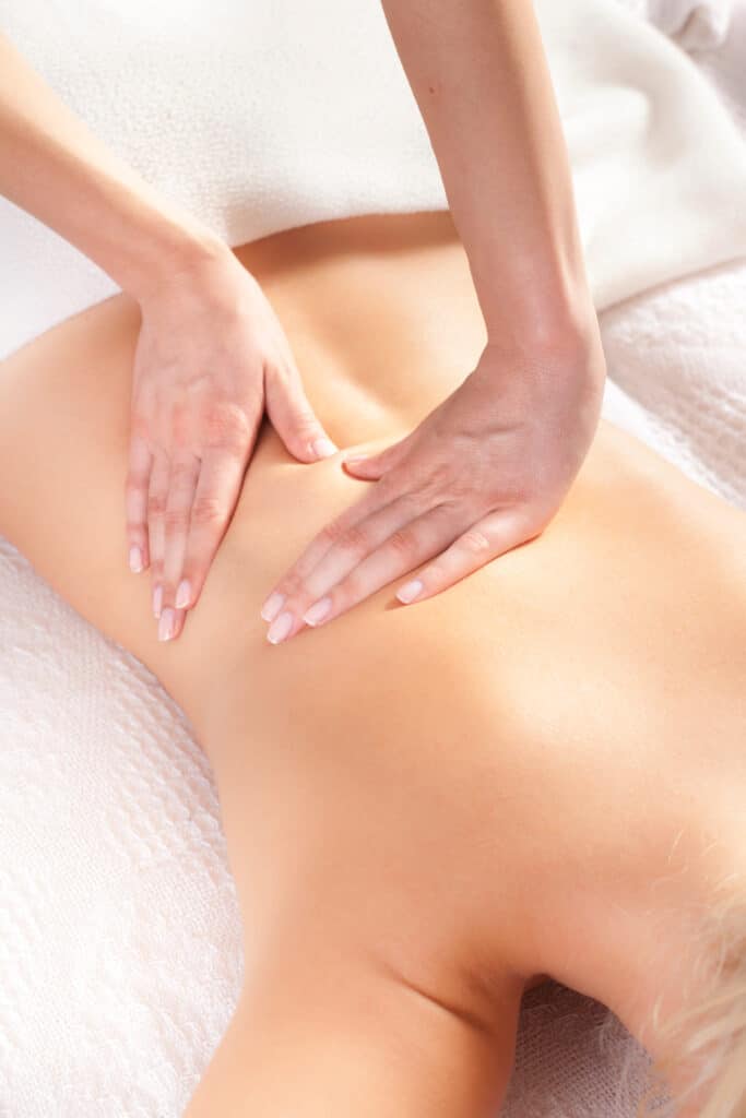 Massage relaxant du dos : soin corps et détente Masseuse appliquant un massage relaxant du bas du dos d'une femme blonde allongée sur une serviette blanche.